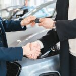 Two businessmen shaking hands and exchanging car keys in a dealership. Symbolizes a successful deal.