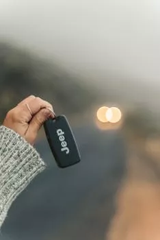 Close-up of a hand holding a car key fob with blurred road background.